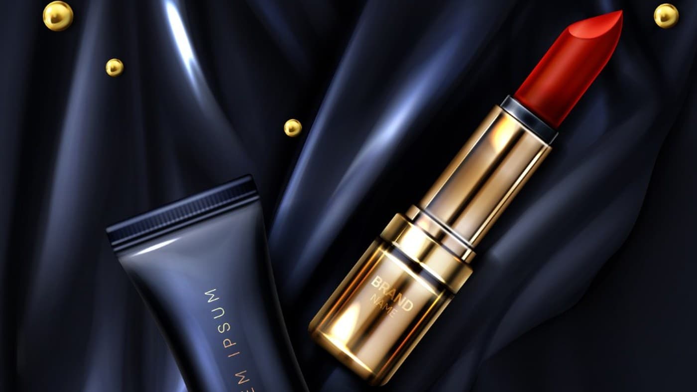 Gold lipstick and black skincare tube on dark satin, scattered with gold pearls