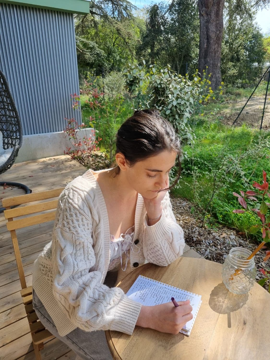 Léa writing in a notebook at a table in a sunny garden