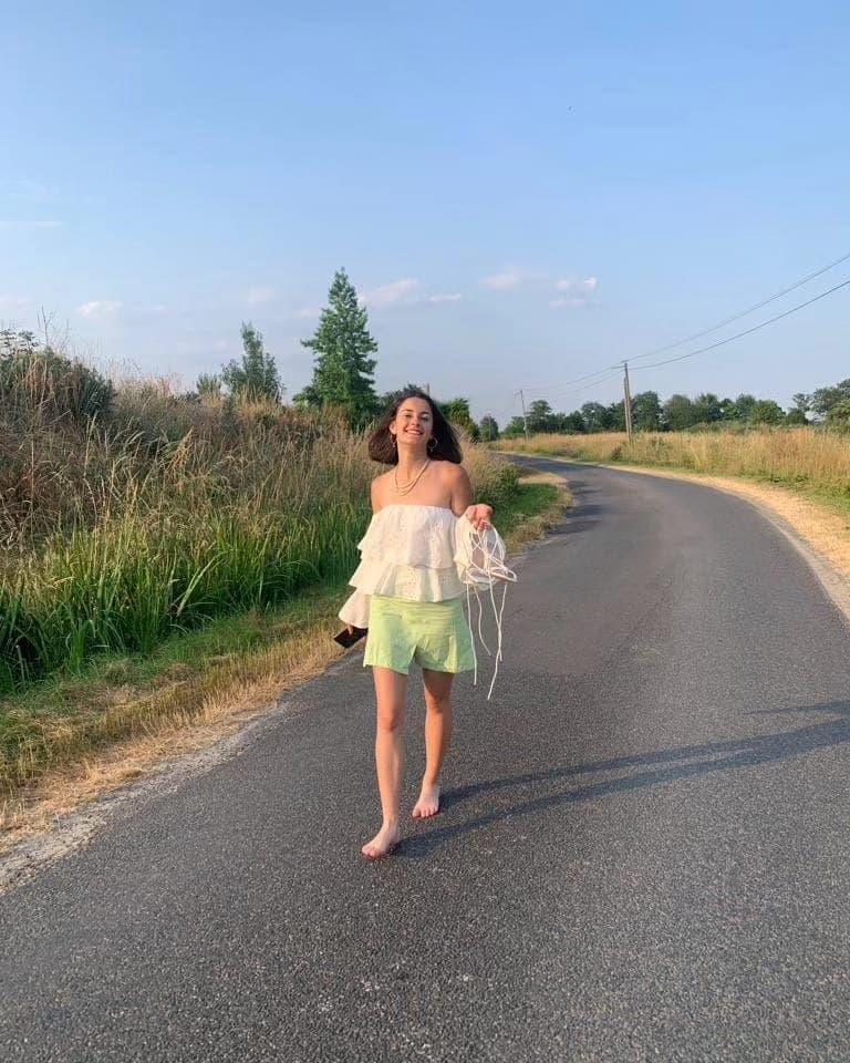 Léa walking barefoot along a country road at golden hour